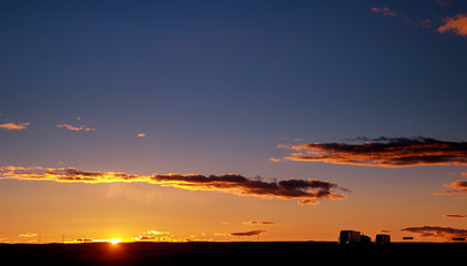 Fototapeta premium Truck cars on a highway at sunrise with beautiful sun in background