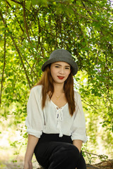 Women white skin lovely brown hair wearing a gray hat red lip wear white shirt wearing black pants women sit poses photography portrait under the tree In the garden.
