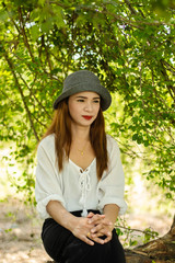Women white skin lovely brown hair wearing a gray hat red lip wear white shirt wearing black pants women sit poses photography portrait under the tree In the garden.