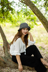 Women white skin lovely brown hair wearing a gray hat red lip wear white shirt wearing black pants women sit poses photography portrait under the tree In the garden.