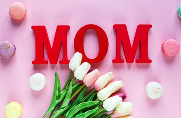 Word Mom from red letters and tender tulips, macaroons on pink background. Mothers day decoration concept. Top view, flat lay with copy space