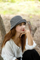 Women white skin lovely brown hair wearing a gray hat red lip wear white shirt wearing black pants women sit poses photography portrait under the tree In the garden.