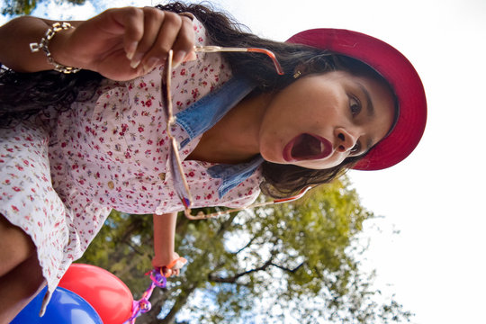 Young girl and very fashionista with floral dress and pink hat is surprised to see something incredible. In his hands he wears sunglasses and balloons.