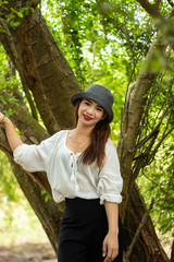 Women white skin lovely brown hair wearing a gray hat red lip wear white shirt wearing black pants women standing poses photography portrait under the tree In the garden.