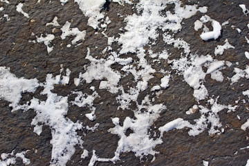 Macro view of white snow texture patterns on top of black asphalt surface