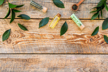 Tea tree oil in small glass bottle near fresh tea tree leaves on rustic wooden background top view space for text border