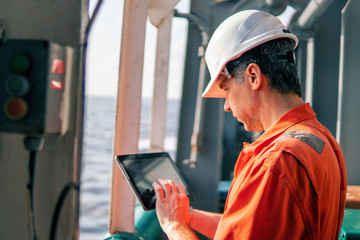 Marine chief officer or captain on deck of vessel or ship watching digital tablet. Internet and...