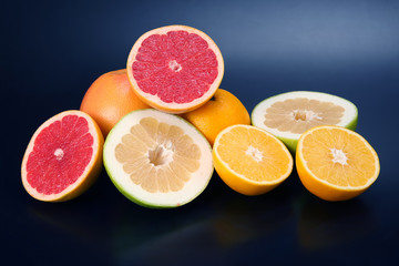 cut pieces of different citrus fruits on dark background