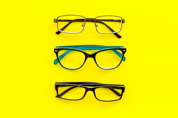 Set of glasses with transparent lenses on yellow background top view