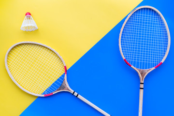 Badminton equipment. Badminton rackets and shuttlecock on yellow and blue background top view copy space