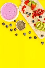 Preparing healthy fruit smoothie. Acai smoothie bowl near cutting board with fresh fruits, berries, chia seeds on yellow background top view space for text