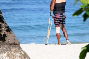Accident tourist man are walking by crutches on the beach while travel