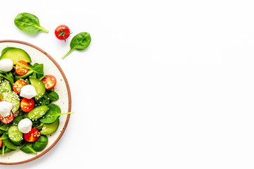 Fresh salad with mozzarella, spinach, cherry tomatoes, cucumber on plate on white background top view copy space
