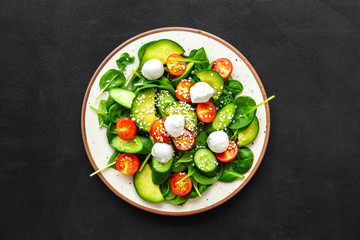 Fresh salad with mozzarella, spinach, cherry tomatoes, cucumber on plate on black background top view space for text