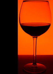 Glass or stemware with alcohol wine,whiskey,gin,beer,rum,vodka,Scotch,cognac,liquor,brandy,absinthe or cocktail on orange background. A glass on the bar in a cafe, restaurant, nightclub or disco.