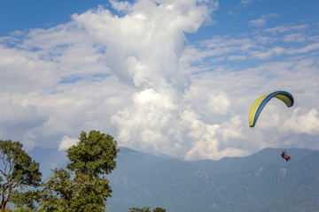 tandem paragliders in the sky against the backdrop of a misty mountain valley and heavy white clouds