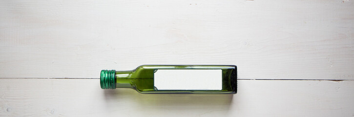 Green bottle for olive oil with white blank sticker for your teat of design. Flat lay, top view with white wooden rustic background. Mock up for product illustration.