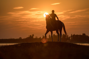 Silhouette  young man riding a horse in the during sunset on the hill lakeside