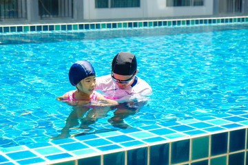 Father teaching daughter swimming in pool