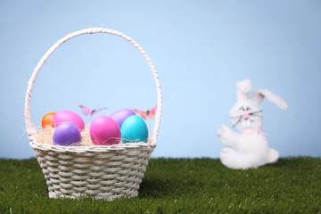 White bunny and wicker basket full of colorful Easter eggs