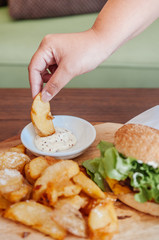 Hand picking fried potato chunks with ranch dipping sauce and hamburger