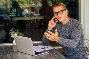 business man using laptop or netbook computer while seated at a cafe table outdoors talking on the phone.remote work