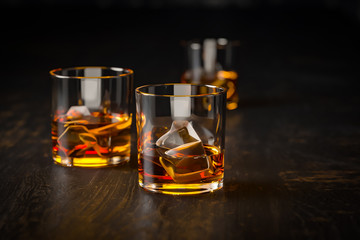 whiskey three glasses with ice, stand on a dark old wooden table and a black background
