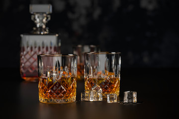 whiskey three glasses with ice, stand on a dark old wooden table on a black background with a carafe