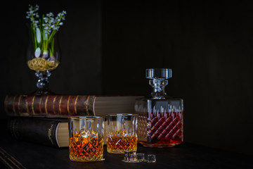 whiskey two glasses with ice and a carafe, stand on a dark old wooden table with old books on a black background