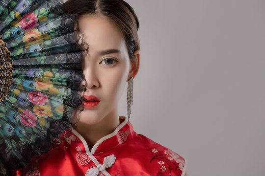 Portrait Of Asian At Traditional Chinese Dress. Close up fashion shot of asian woman holding Chinese fan look at camera on grey background free from copy space. Chinese new year concept