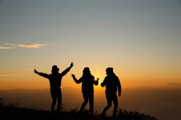 Fototapeta na wymiar Silhouette of young woman are standing on top of the mountain with raised hands relaxing with sunrise by nature at sunrise, Life style, Group of happy at sunrise or sunset, First morning light