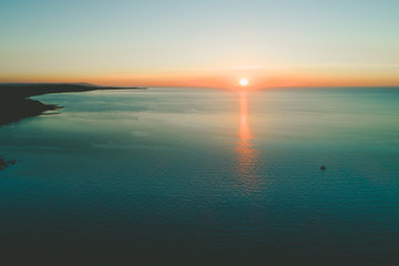 Obraz premium Lonely boat in the vast ocean near the coastline at sunset. Aerial view with copy space