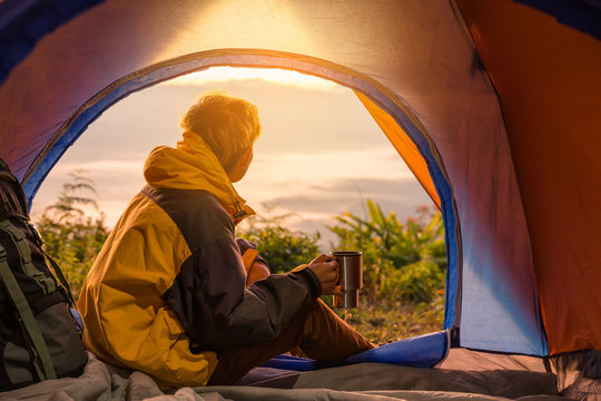 A young man sitting in the tent with holding coffee cup, looking at the mountain landscape in winter.Light effects