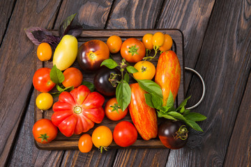 A mix of sliced and whole tomatoes on a rustic wooden board