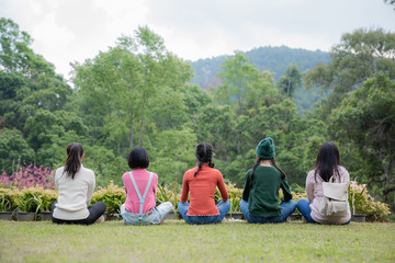 Group of friends sitting together on greensward and enjoying themselves. Young women enjoying on...