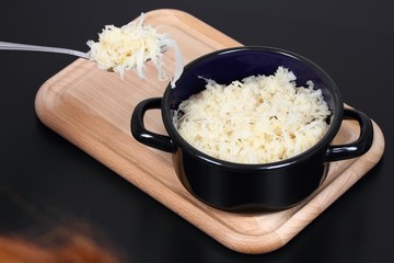 Sauerkraut on a fork and in a pot.  Sauerkraut (fermented or pickled cabbage) on a chopping board, black background