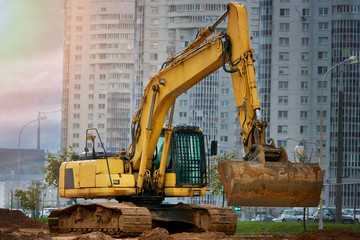Yellow heavy duty digger on background of residential complex. Large excavator bucket collect and...