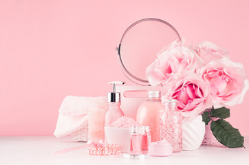 Delicate girlish dressing table with bouquet of roses, round mirror, cosmetic products for body and skin care in pastel pink color on white wood board, copy space.