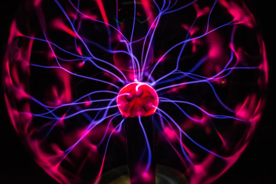 Electric plasma globe with blue energy filaments striking inner surface of glass globe causing red glow.