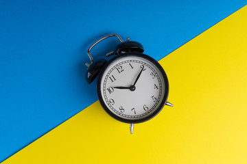 Black vintage alarm clock on a blue and yellow background with selective focus