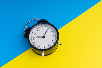 Black vintage alarm clock on a blue and yellow background with selective focus