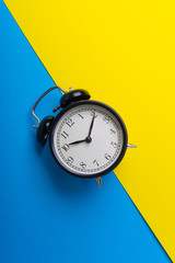 Black vintage alarm clock on a blue and yellow background with selective focus