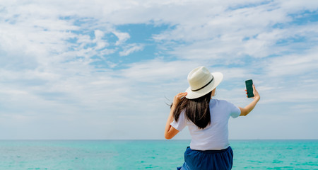 Young Asian woman wear straw hat use smartphone taking selfie at wooden pier. Summer vacation at...