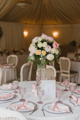 Coziness and style. Modern event design. Table setting at wedding reception. Floral compositions with beautiful flowers and greenery, candles, laying and plates on decorated table.