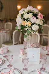 Coziness and style. Modern event design. Table setting at wedding reception. Floral compositions with beautiful flowers and greenery, candles, laying and plates on decorated table.