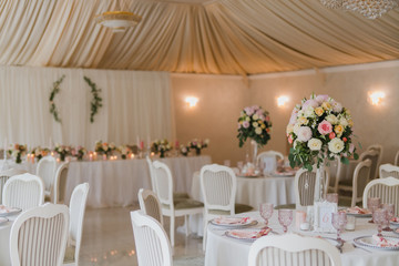 Coziness and style. Modern event design. Table setting at wedding reception. Floral compositions with beautiful flowers and greenery, candles, laying and plates on decorated table.