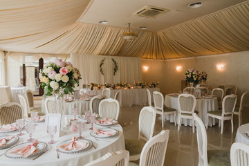 Coziness and style. Modern event design. Table setting at wedding reception. Floral compositions with beautiful flowers and greenery, candles, laying and plates on decorated table.