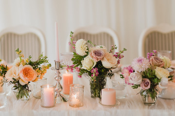 Coziness and style. Modern event design. Table setting at wedding reception. Floral compositions with beautiful flowers and greenery, candles, laying and plates on decorated table.