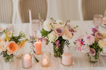 Coziness and style. Modern event design. Table setting at wedding reception. Floral compositions with beautiful flowers and greenery, candles, laying and plates on decorated table.