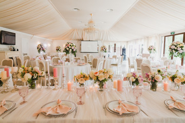 Coziness and style. Modern event design. Table setting at wedding reception. Floral compositions with beautiful flowers and greenery, candles, laying and plates on decorated table.